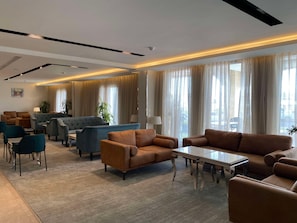 A hotel lobby with a seating area, a coffee table, and large windows with curtains.
