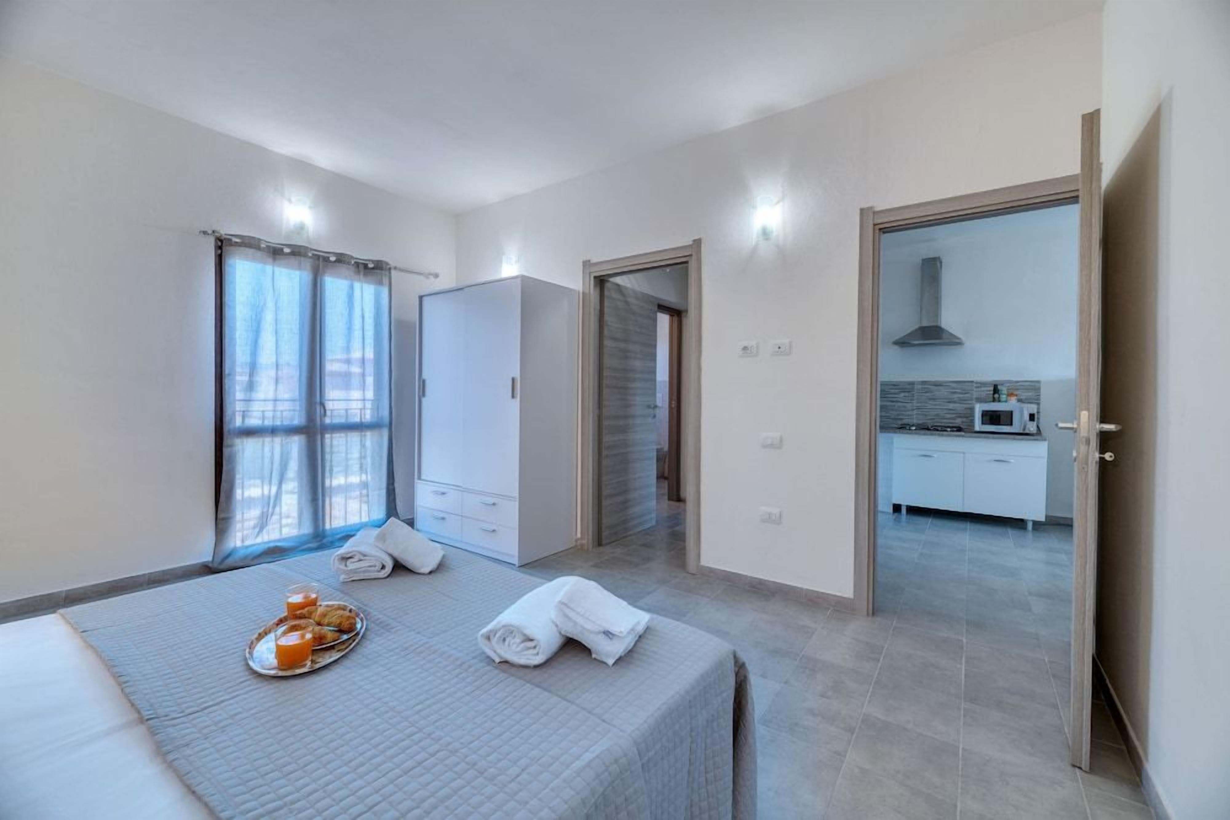 A modern bedroom with a bed, a breakfast tray, and a view of a kitchen.
