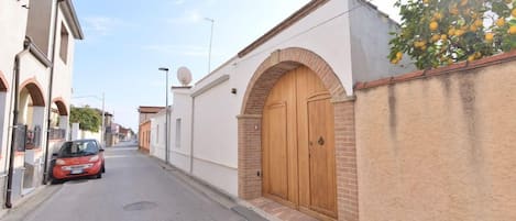 A narrow street with a parked car and a building with a large wooden door.