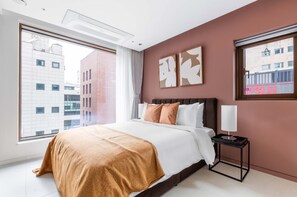 Ein Hotelzimmer mit einem großen Bett, einem Nachttisch, einem Fenster mit Stadtblick und Kunstwerken an der Wand.