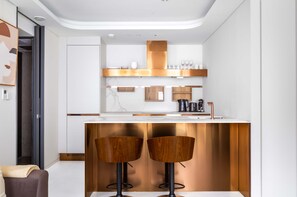 Une cuisine moderne avec un plan de travail blanc, des tabourets de bar en bois et un four encastré.