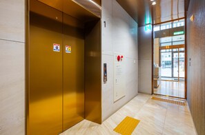 Interior de elevador com placas de saída de emergência, alarme de incêndio e indicador de andar.