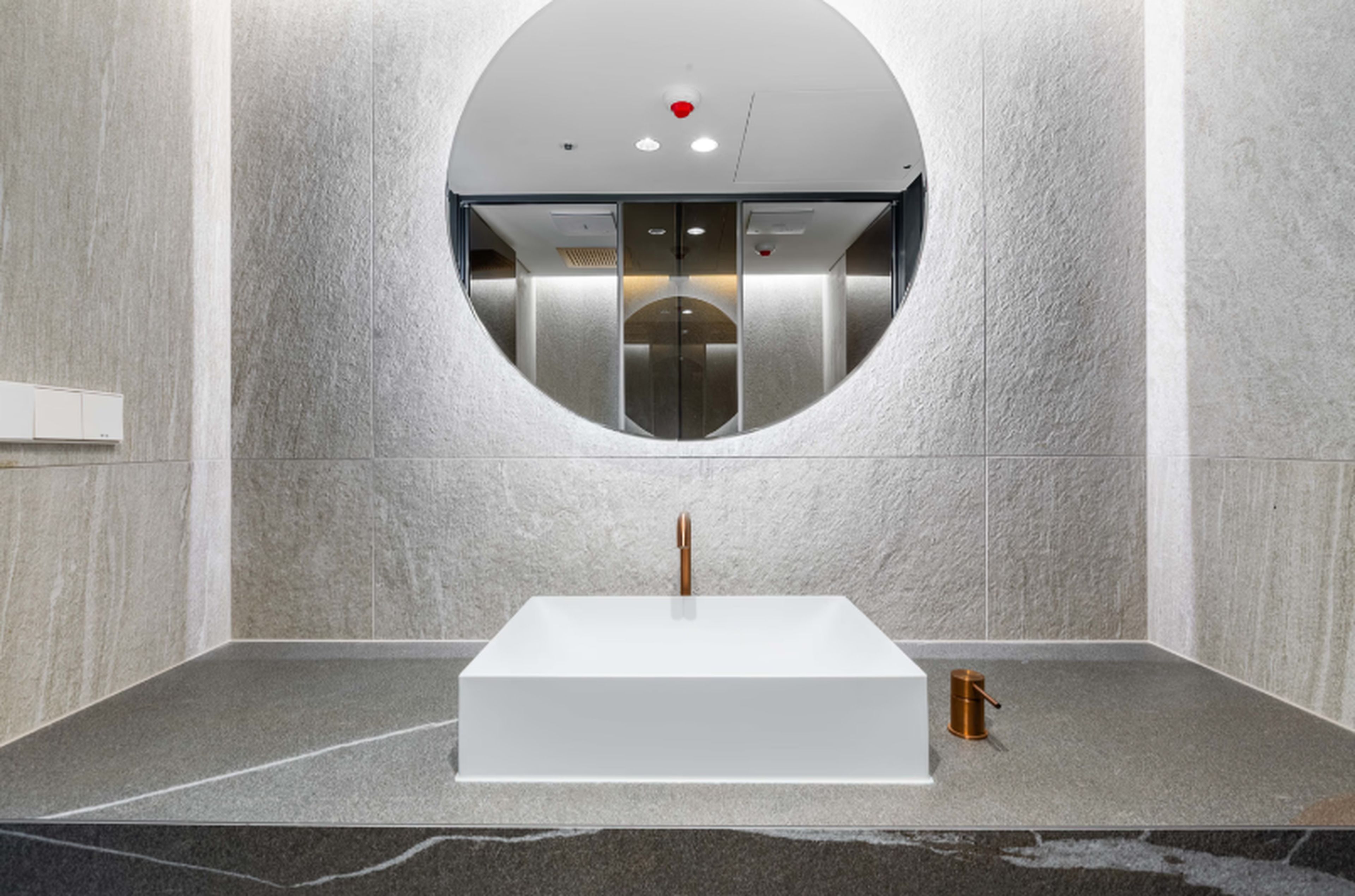 A modern bathroom with a central sink, a circular mirror, and a wall-mounted toilet.