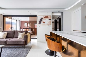 A modern living room with a sofa, a coffee table, and a dining area with a bar. - Luxia Dosan - Executive Suite - Fully Furnished 1BR 1B (Seoul)