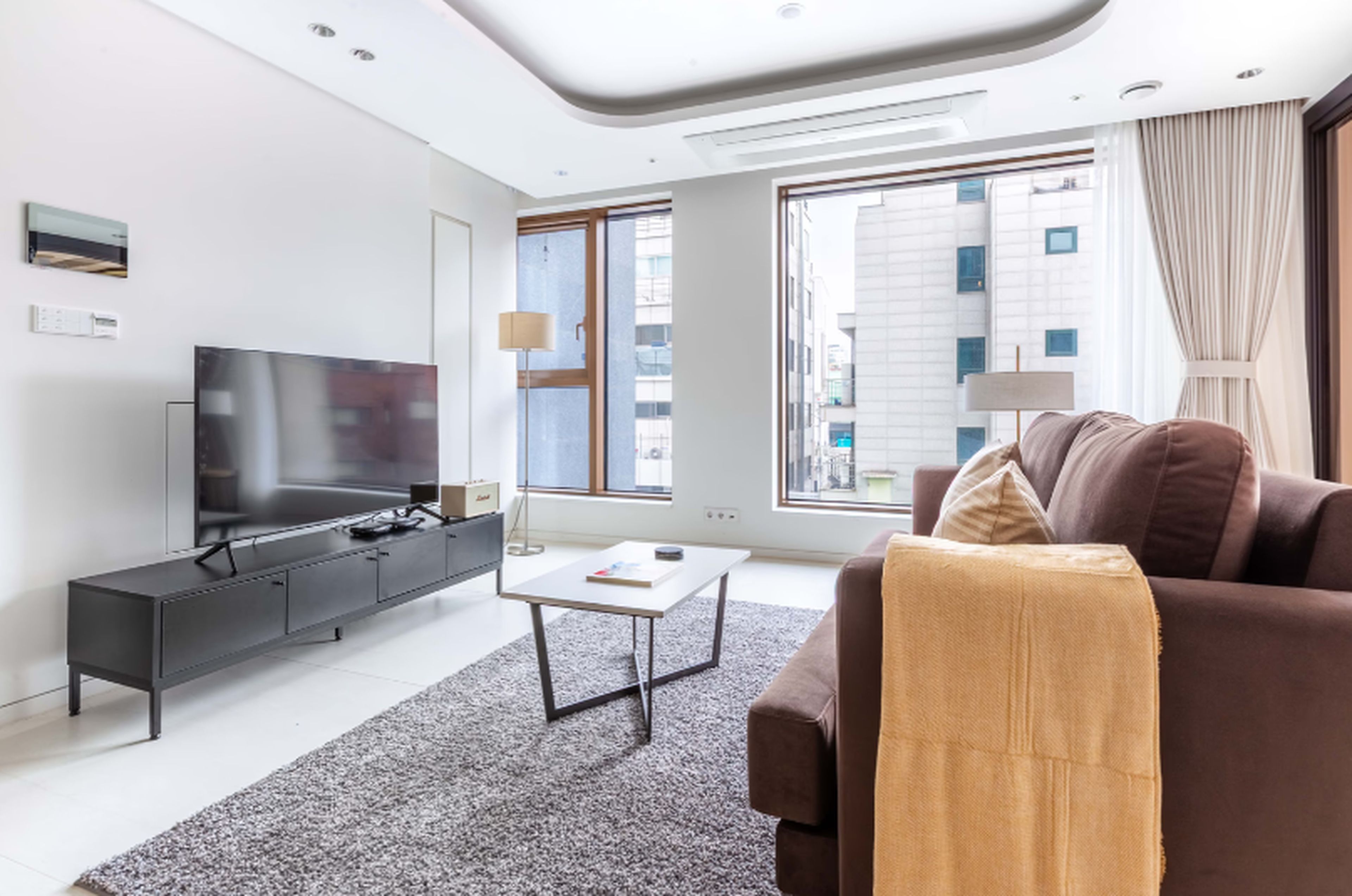 A modern living room with a flat-screen TV, a sofa, a coffee table, and a large window with a city view.