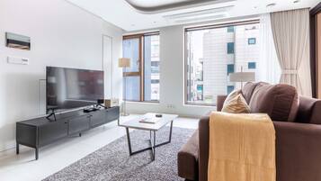 A modern living room with a flat-screen TV, a sofa, a coffee table, and a large window with a city view.