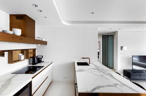 Une cuisine moderne dotée d’un plan de travail en marbre, d’appareils électroménagers intégrés et d’une étagère en bois au-dessus de l’évier.
