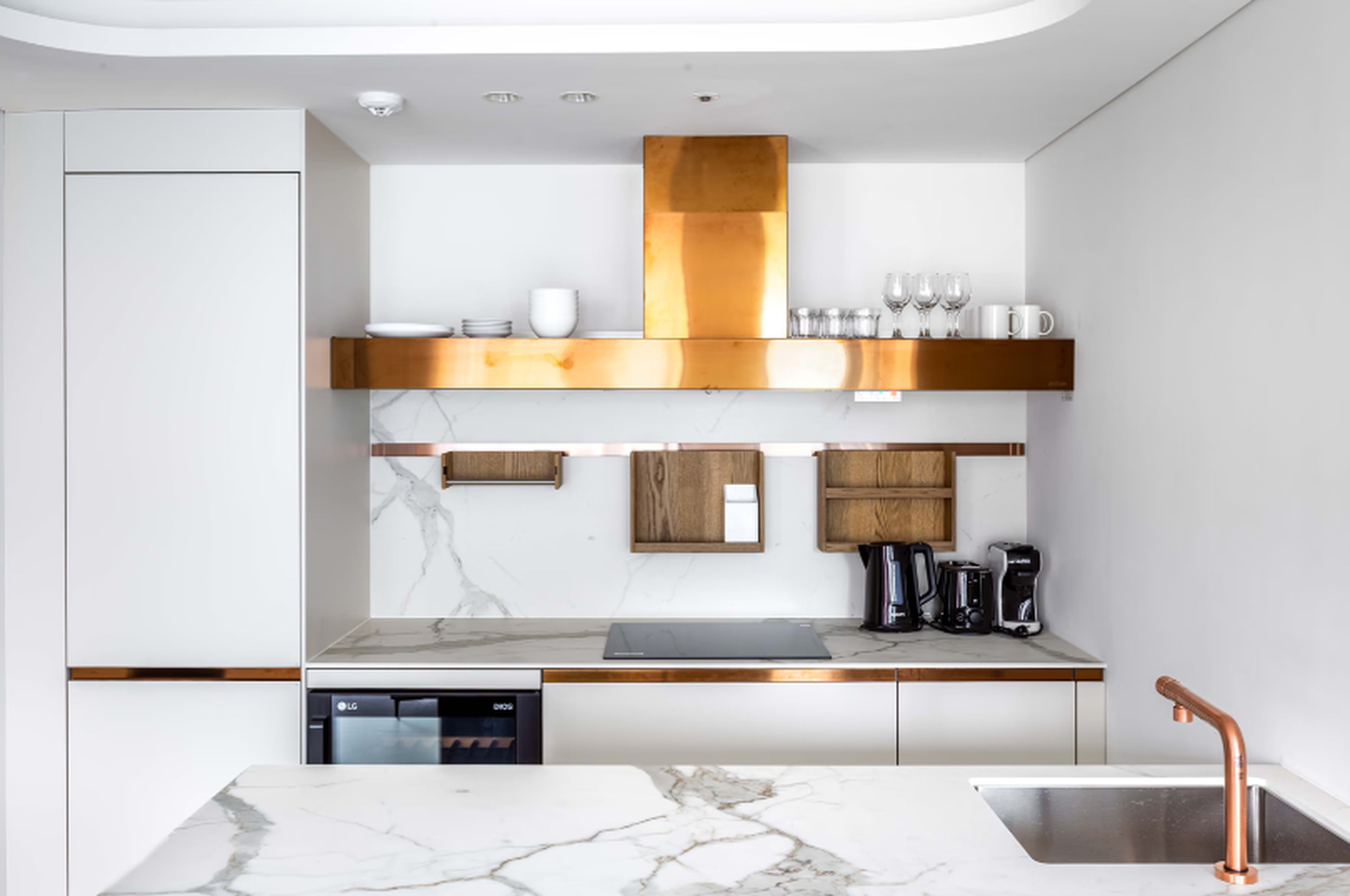 A modern kitchen with a marble countertop, stainless steel sink, and a copper faucet.