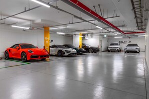 Un parking souterrain où sont garées plusieurs voitures, dont une voiture de sport rouge, et un panneau indiquant la sortie avec une flèche pointant vers la droite.