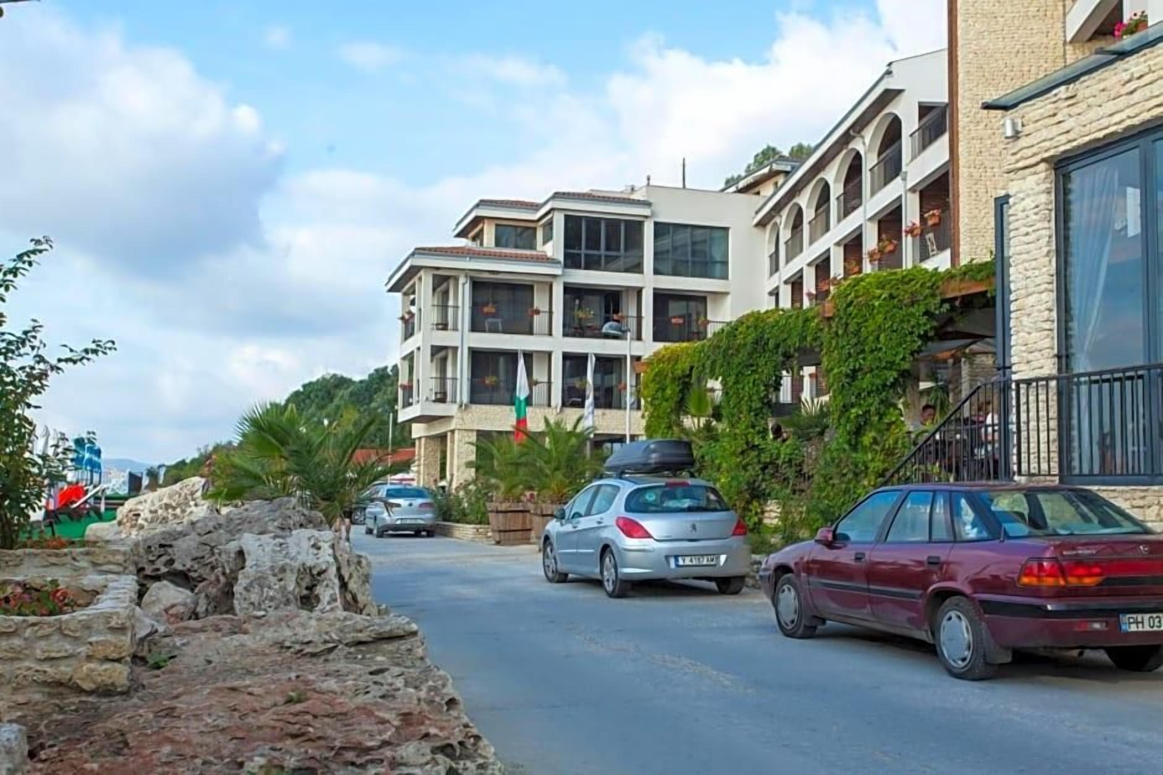A street with modern buildings, parked cars, and a clear sky.