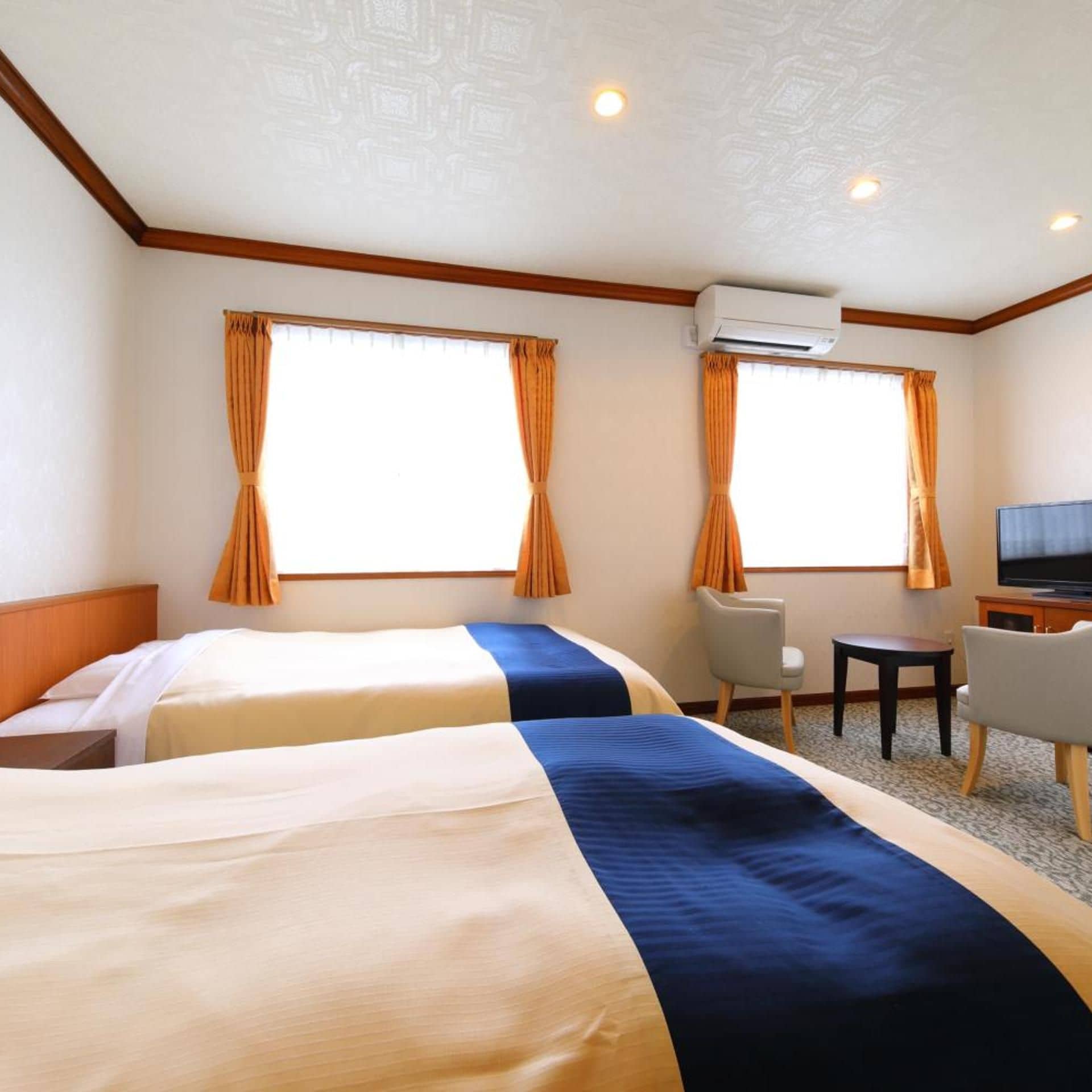Habitación de hotel con dos camas, televisión, escritorio y aire acondicionado.