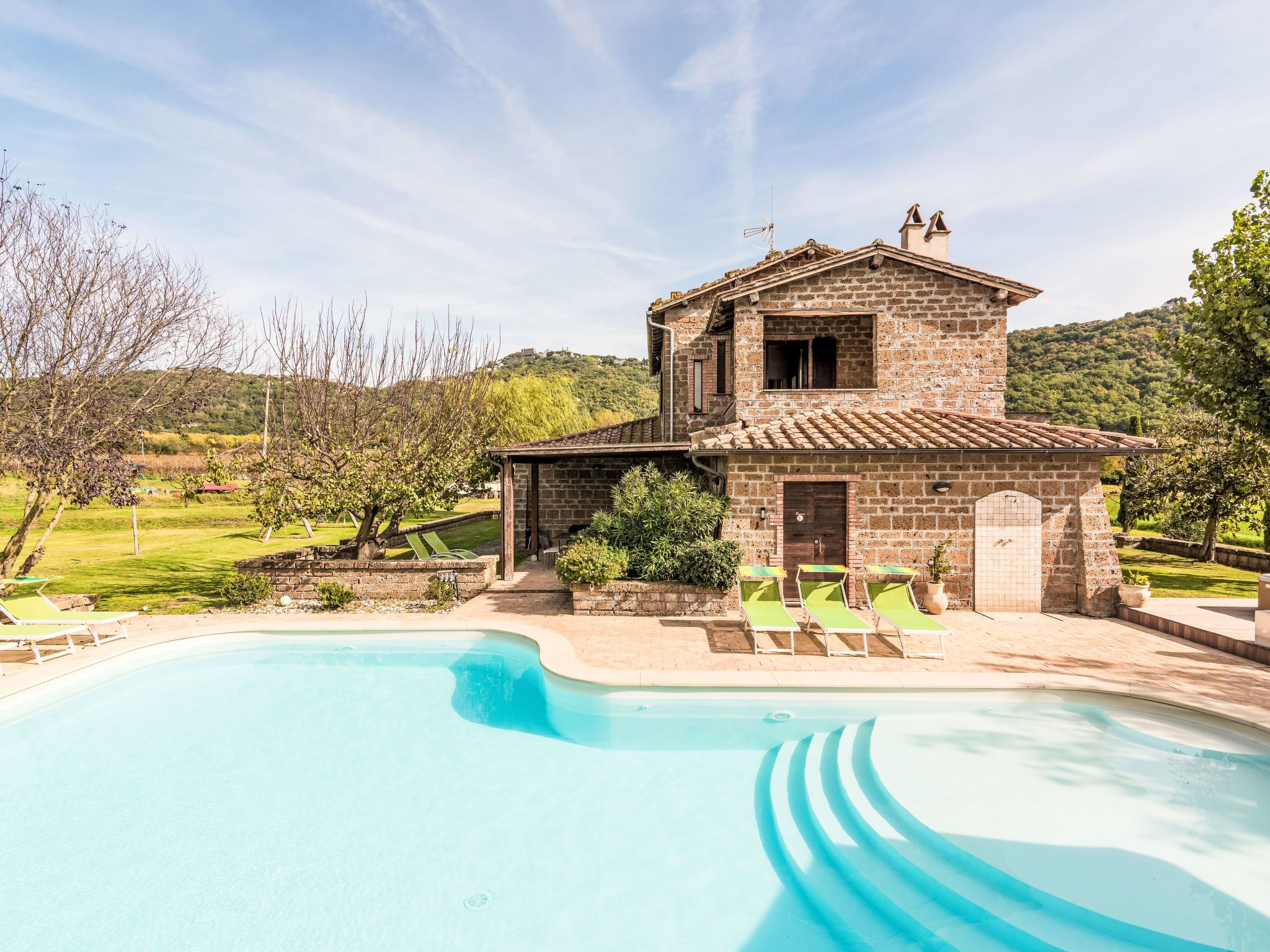 A two-story stone house with a swimming pool in front.