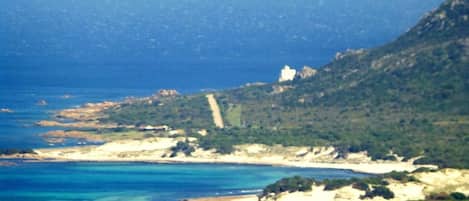 A coastal landscape with a beach, clear blue waters, and a mountainous backdrop.