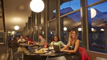 A restaurant with tables and chairs, large windows, and a view of mountains.