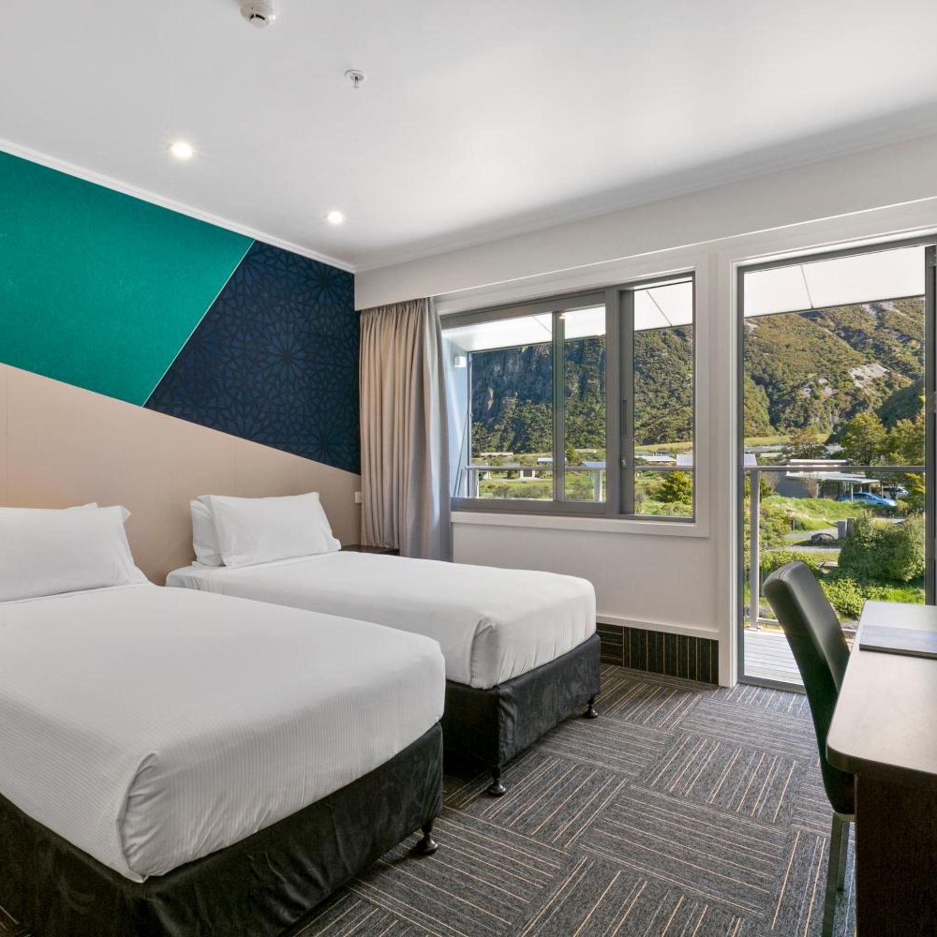 A hotel room with two beds, a large window with a mountain view, and a modern design.