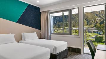 A hotel room with two beds, a large window with a mountain view, and a modern design.