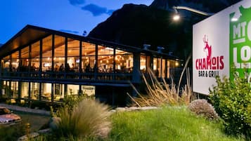A modern building with a glass facade, a sign for 'Chaimois Bar & Grill,' and a mountain backdrop.