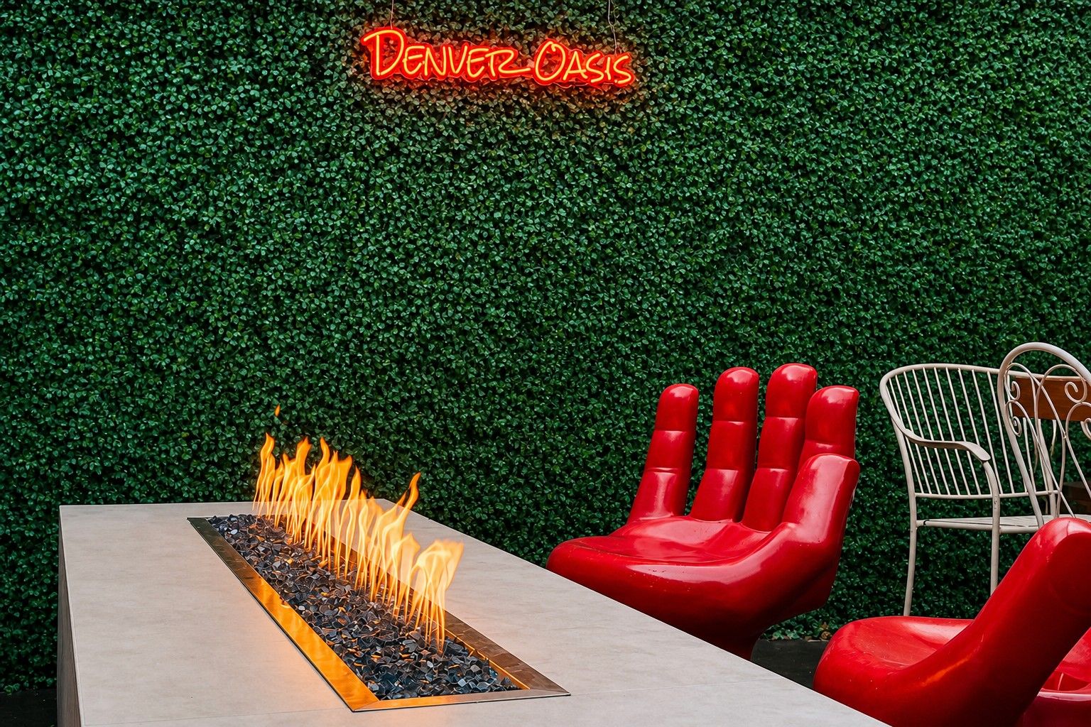 A modern outdoor seating area with a neon sign, a fire feature, and red chairs.