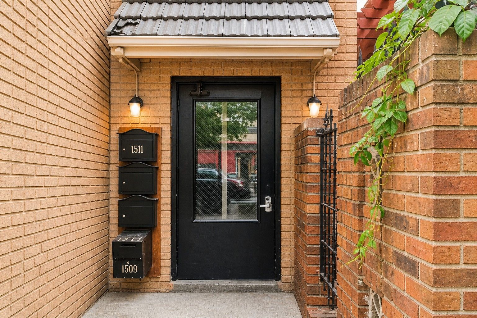 A black door with a glass panel, a mailbox with numbers 1511 and 1509, and a small step leading to the door.