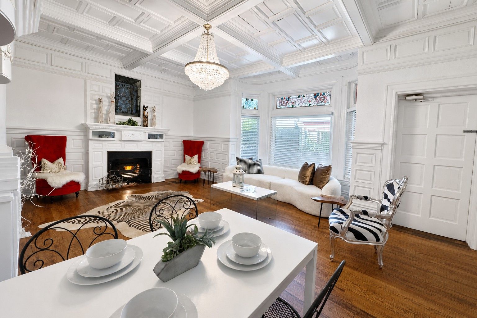 A spacious living room with a fireplace, a dining area with a table set for four, and a large chandelier.
