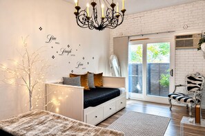 A bedroom with a bed, a chandelier, a white wall with decorative text, a window, and a chair. - Unique style condo with HOT TUB! (Denver)