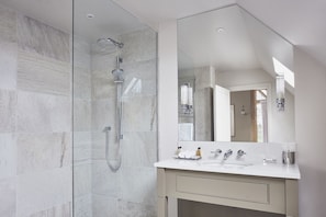 A modern bathroom with a glass-enclosed shower, a white vanity with a mirror, and a door leading to another room.