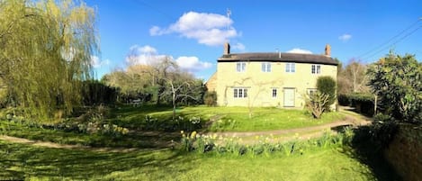 A two-story house with a garden, a pathway, and a small pond.