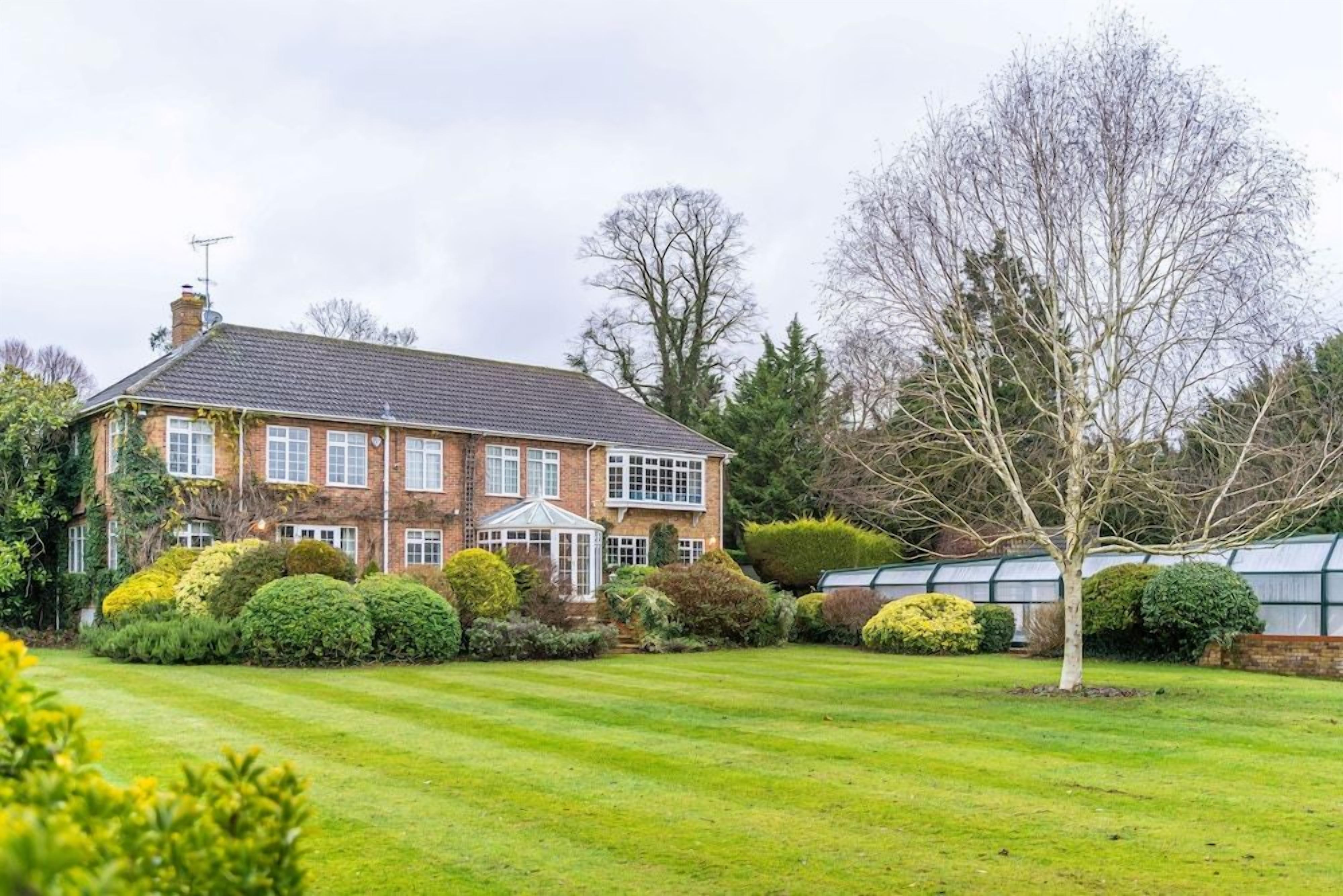 A large brick house with a conservatory, surrounded by well-maintained lawns and hedges.