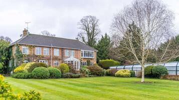 A large brick house with a conservatory, surrounded by well-maintained lawns and hedges.