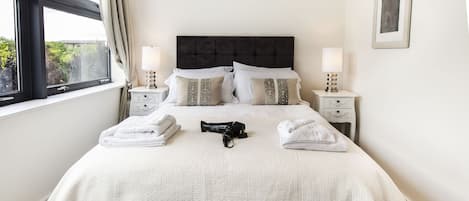 A neatly made bed with white linens, two bedside tables with lamps, and a framed picture on the wall.