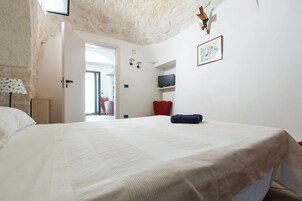 Un dormitorio con una cama grande, televisor, una silla roja y una puerta que da a otra habitación.