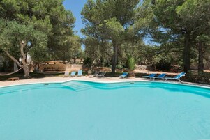 Una piscina con sillas de descanso y árboles al fondo.
