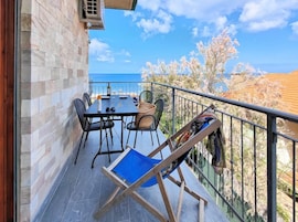 A balcony with a table and chairs, a blue folding chair, and a view of the sea.