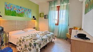 Quarto de hotel com cama, escrivaninha, cadeira, quadro na parede e janela com cortinas.