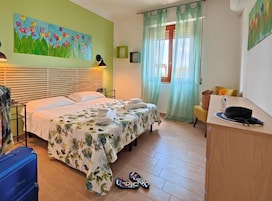A hotel room with a bed, a desk, a chair, a painting on the wall, and a window with curtains.