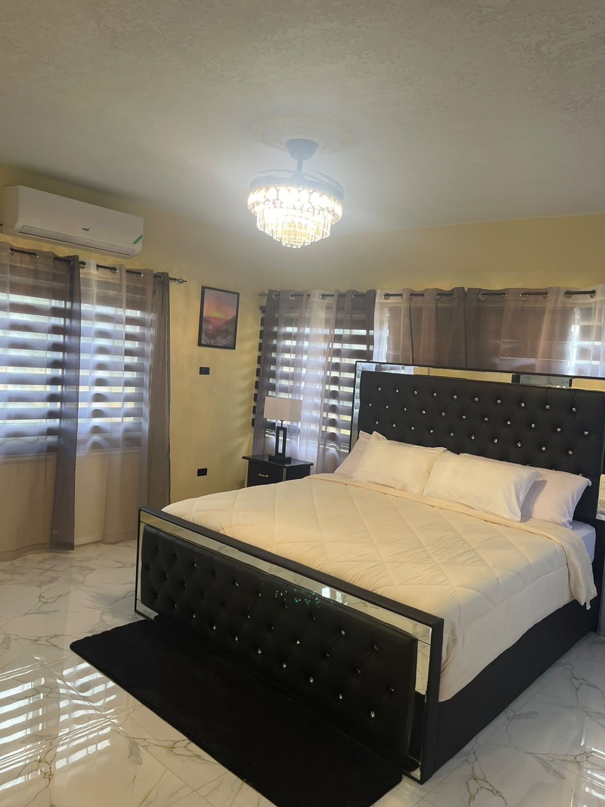 A bedroom with a bed, a chandelier, curtains, and a marble floor.
