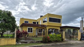 A two-story yellow building with a gated entrance, a small garden, and a tree. - R&R Rest & Restore (Bogwalk)