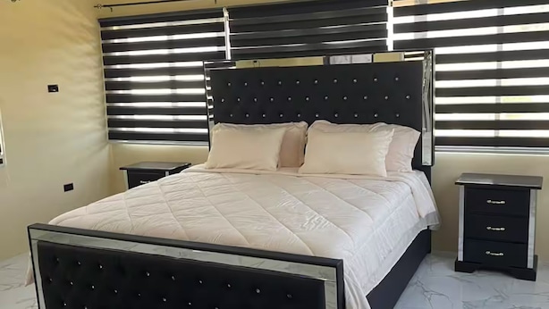 A bedroom with a large bed, a nightstand, a dresser, and a chandelier. - R&R Rest & Restore (Bogwalk)