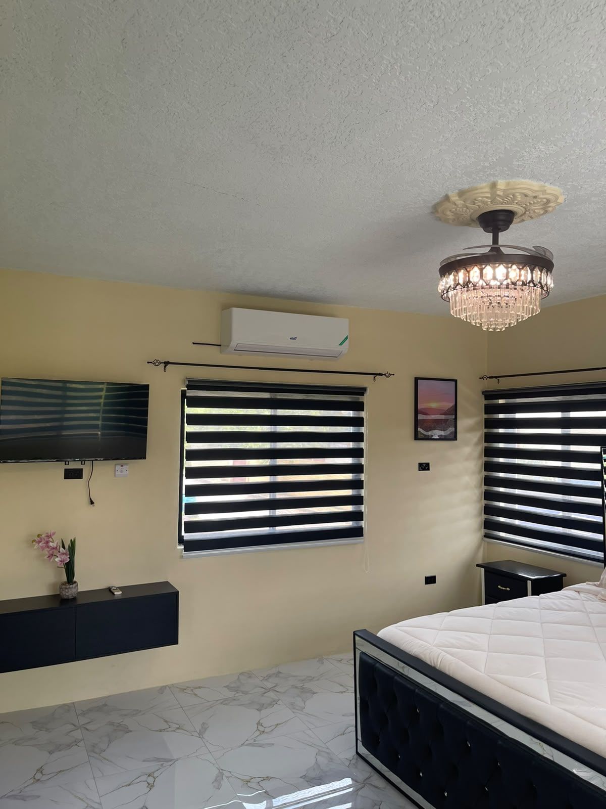 Een slaapkamer met een bed, een airconditioning, een televisie en een kroonluchter.