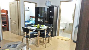 A compact room with a dining table set for two, a black bookshelf, a bed with a colorful bedspread, and a toilet.