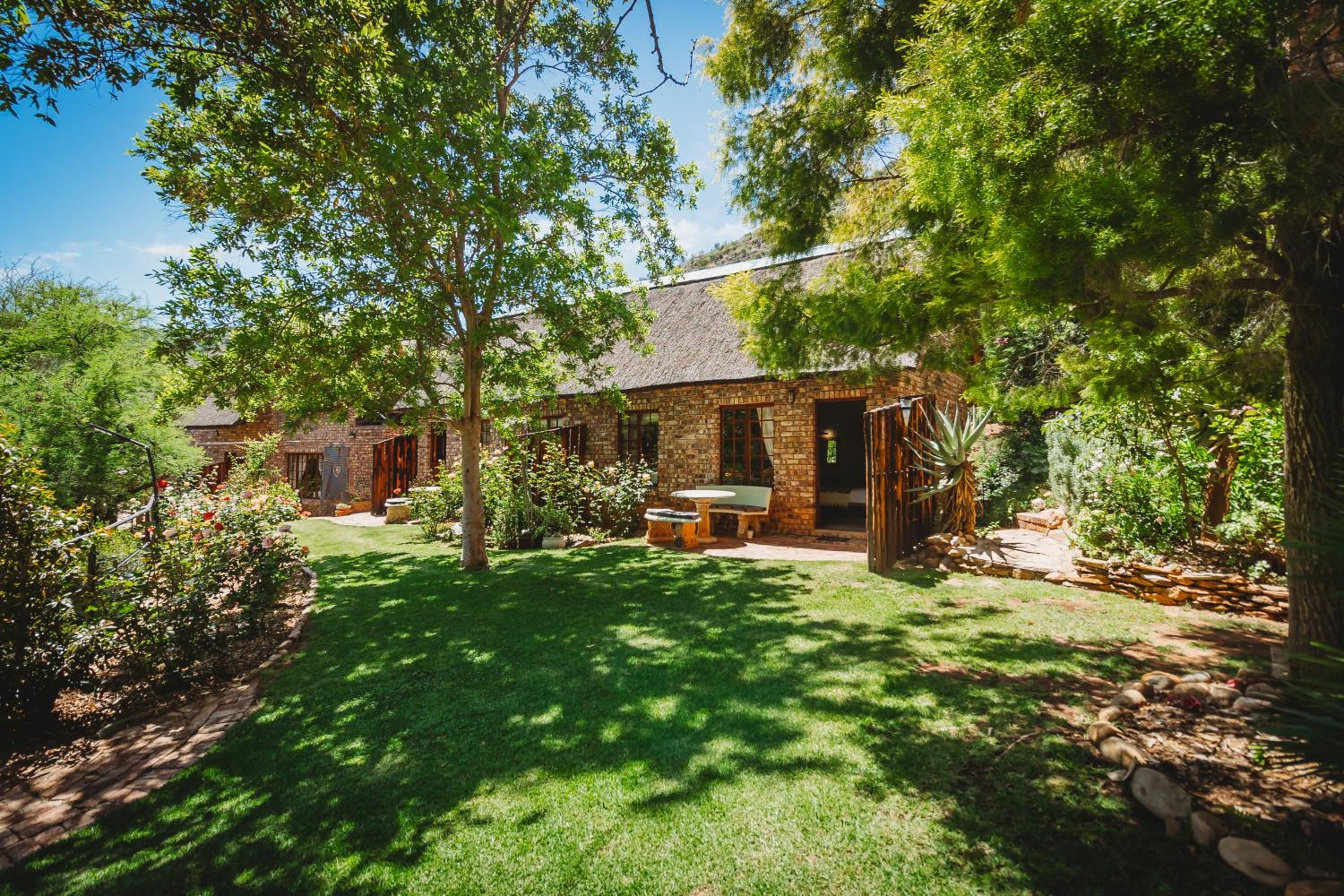 A stone house with a thatched roof, surrounded by a well-maintained garden with a lawn and various plants.