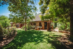 A stone house with a thatched roof, surrounded by a well-maintained garden with a lawn and various plants.