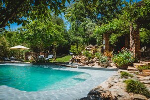 A swimming pool surrounded by lush greenery and a brick structure.