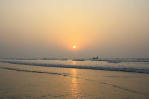 A beach scene with the sun low on the horizon, reflecting on the water. - Le Roi (Kanthi)