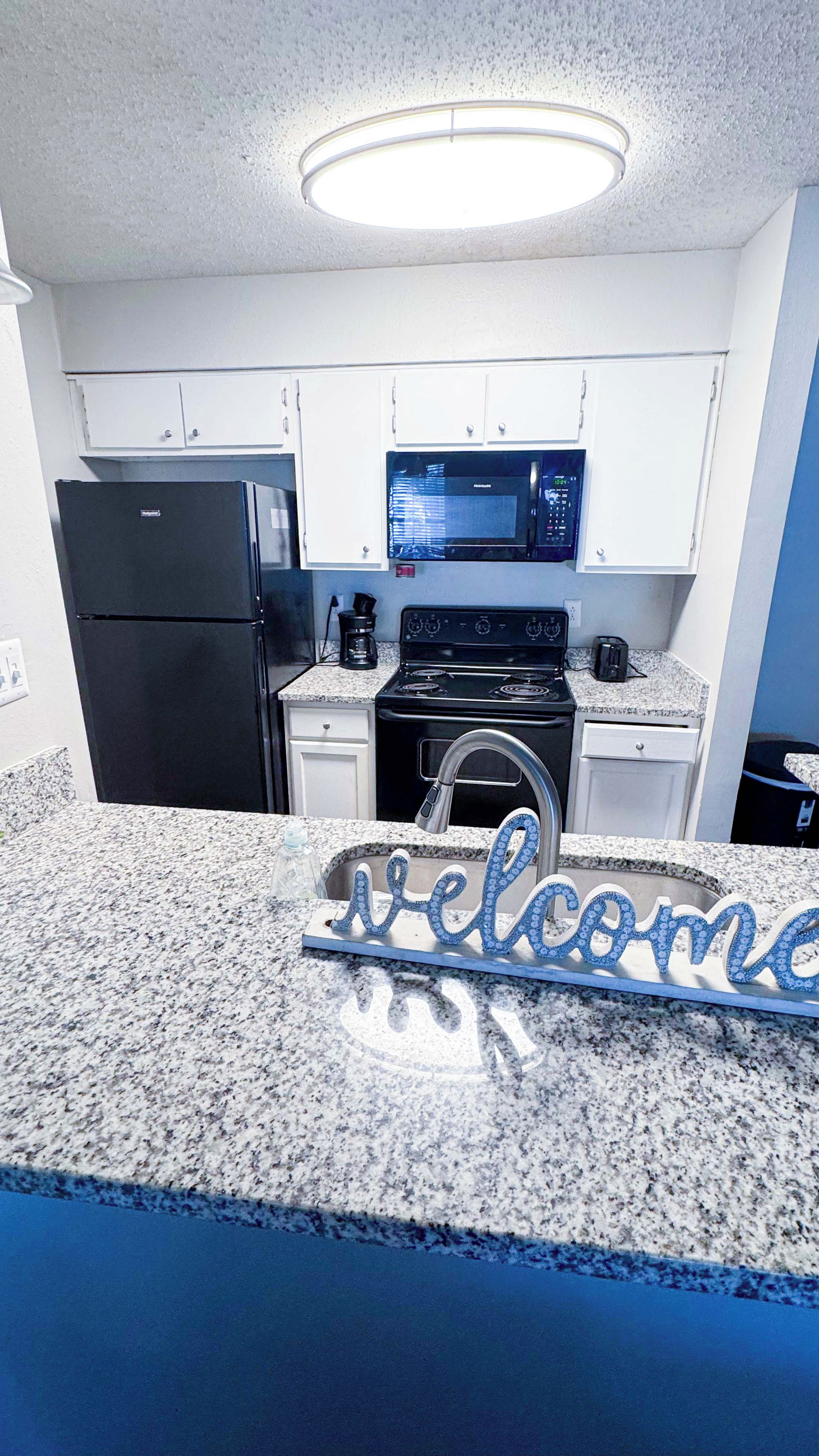 A kitchen with white cabinets, a black refrigerator, a microwave, and a stove.