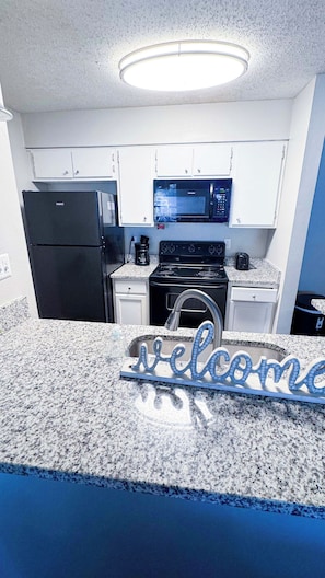 A kitchen with white cabinets, a black refrigerator, a microwave, and a stove.