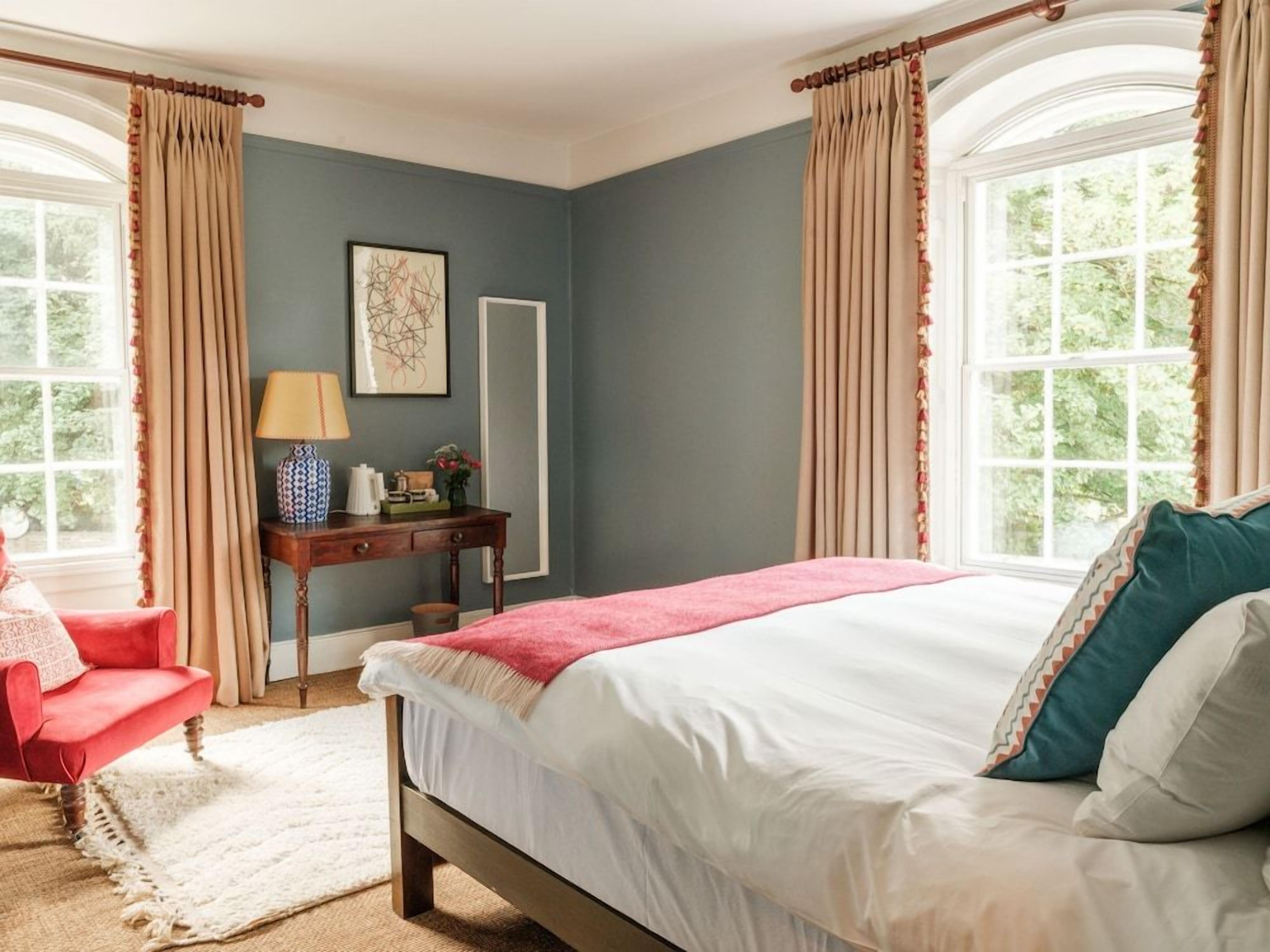 A bedroom with a bed, a desk, a chair, and curtains.