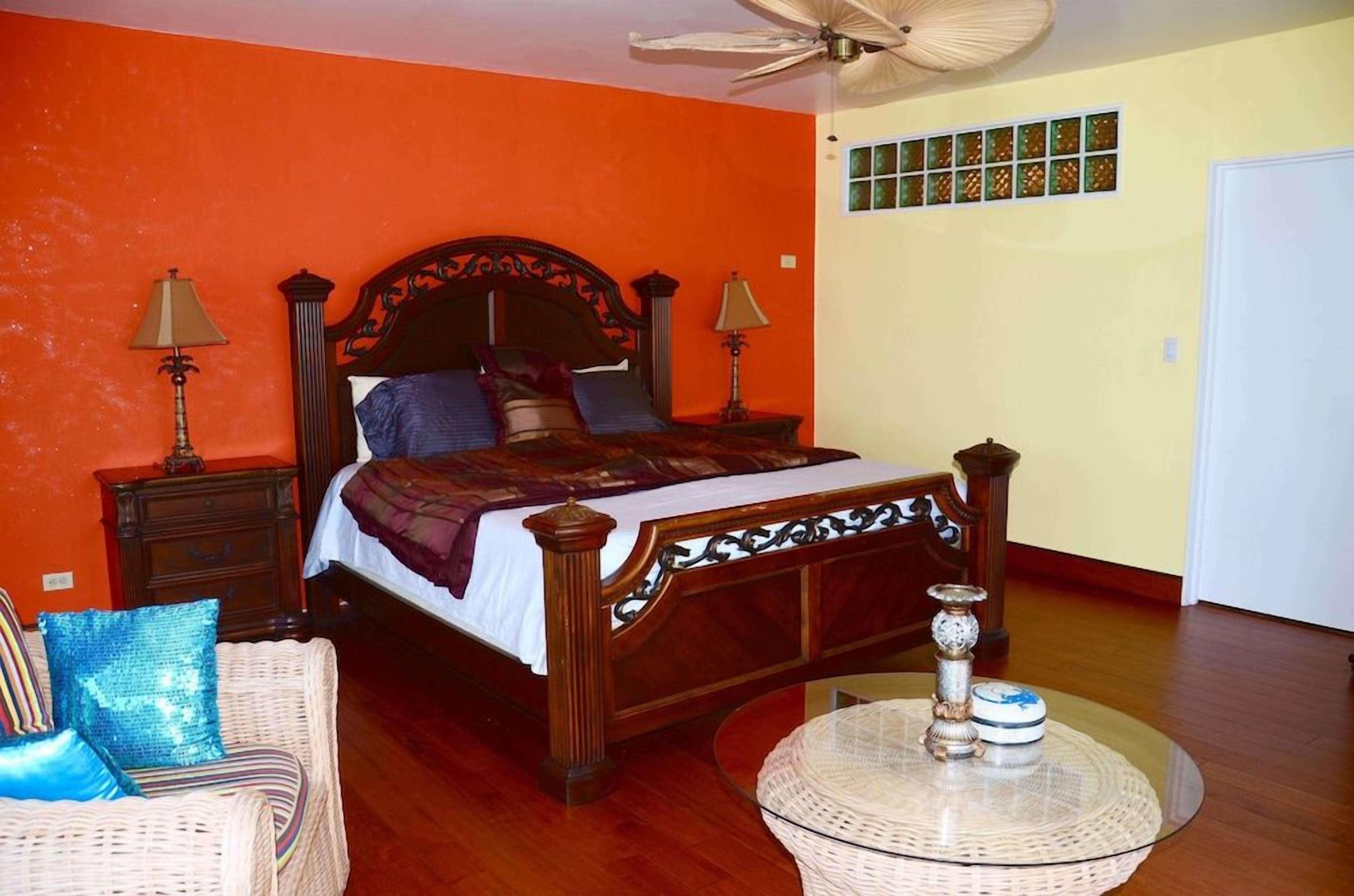 A bedroom with a wooden bed, two bedside tables, a wicker chair, and a round table with a decorative item.