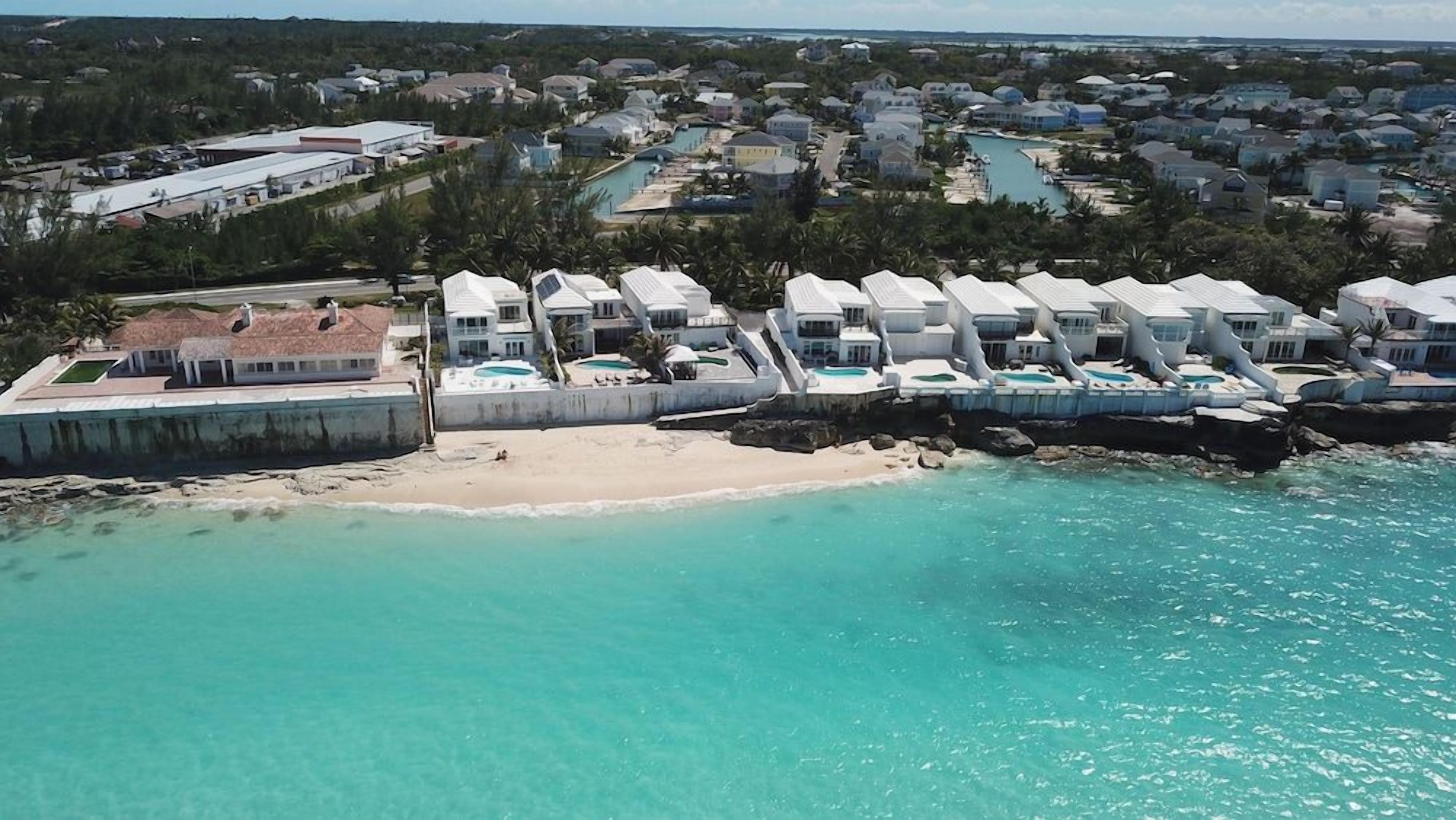 A coastal area with a row of white buildings, some with attached swimming pools, and a sandy beach.