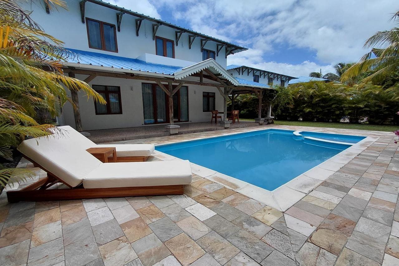 Piscina com espreguiçadeiras, um alpendre coberto e uma casa com telhado azul.
